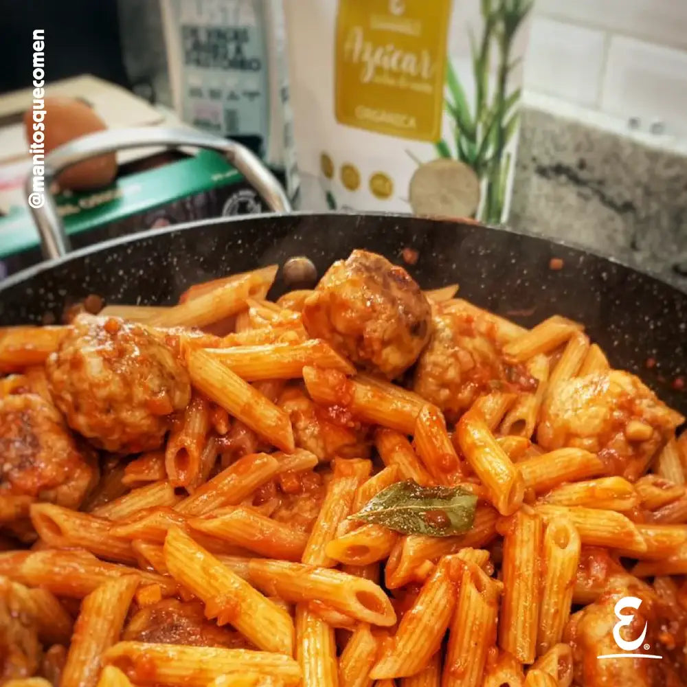 Sartén con albóndigas de cerdo caseras y fideos penne en salsa de tomate natural, junto a empaque de Azúcar Orgánica Ecoterra y huevos de gallinas libres a pastoreo.