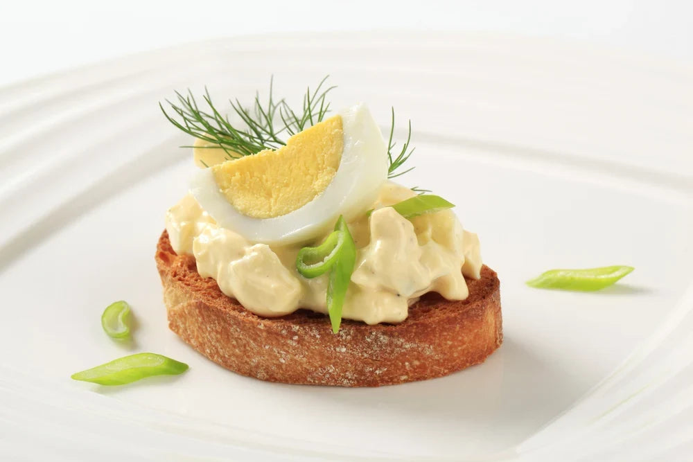 Canapé de tostada crujiente con pasta cremosa de huevo duro de gallina libre a pastoreo Ecoterra, decorado con trozo de huevo y ciboulette fresco.