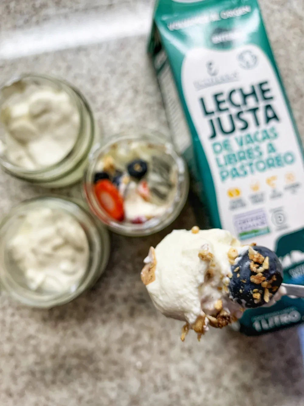 Parfait de leche entera de vacas libres a pastoreo Ecoterra servido con arandanos y granola junto al envase Leche Justa.