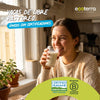 Mujer sonriente bebiendo un vaso de Leche Ecoterra de vacas libres a pastoreo en su cocina, junto a los sellos de certificación Certified Humane y Empresa B.